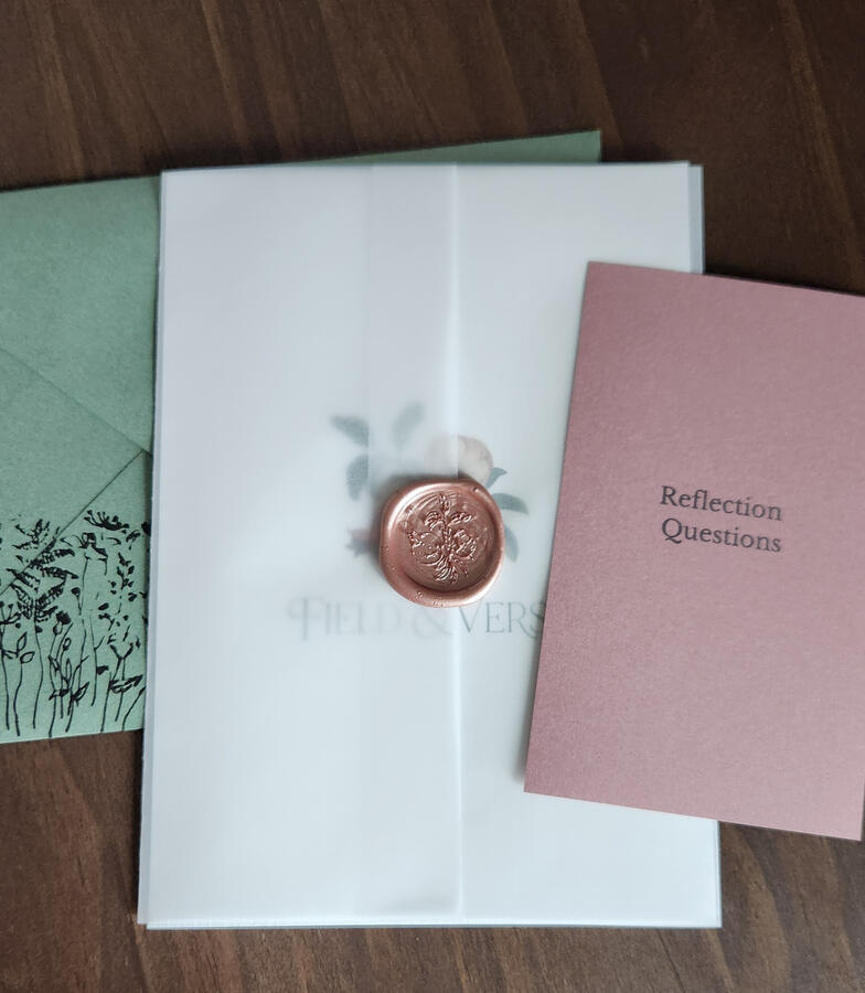 Untitled Image of a green envelope with a Field & Verse print enclosed in vellum wrap with a pink wax seal and a smaller pink card with reflection questions.